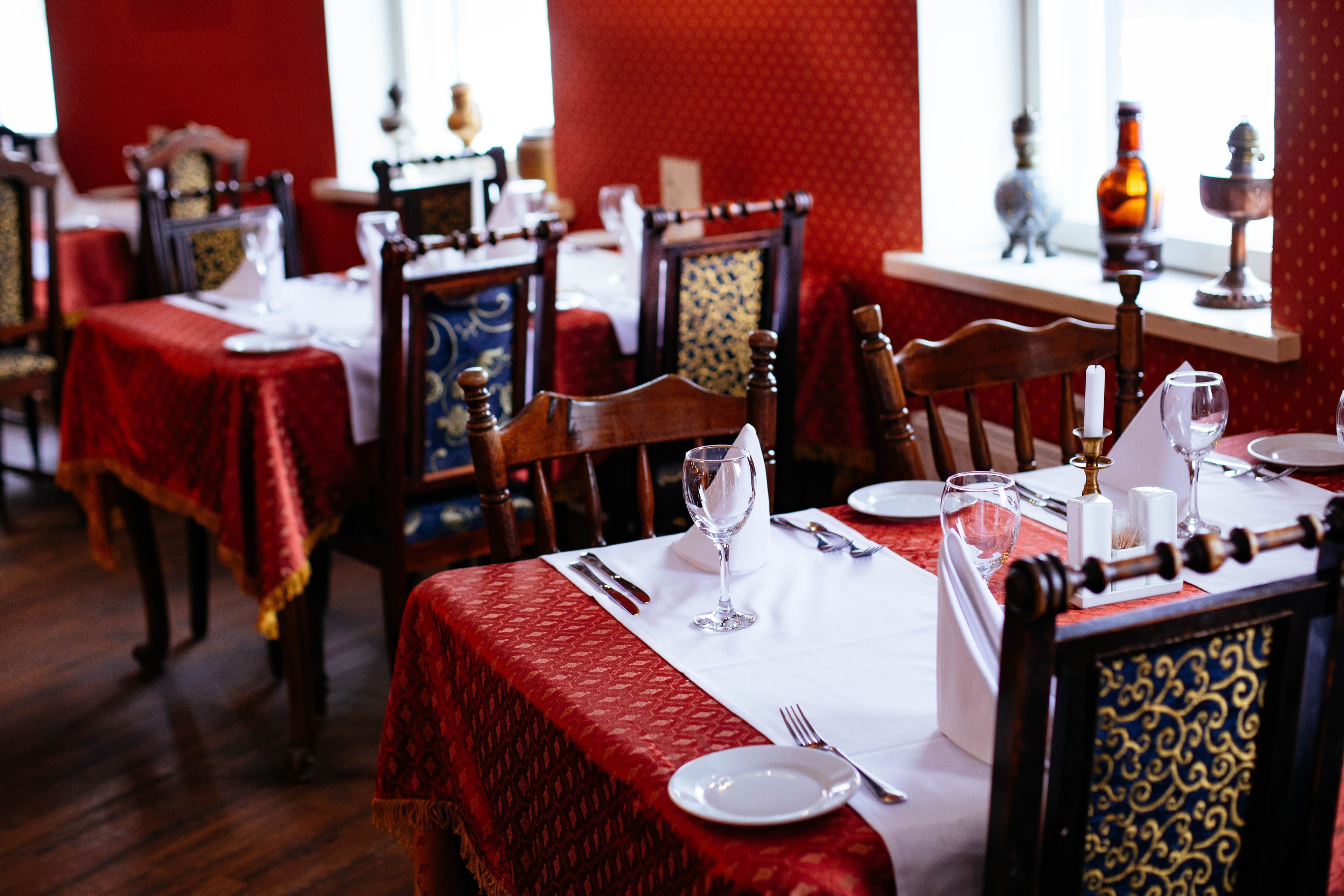 Restaurant tables set with white runners and wine glasses against red walls